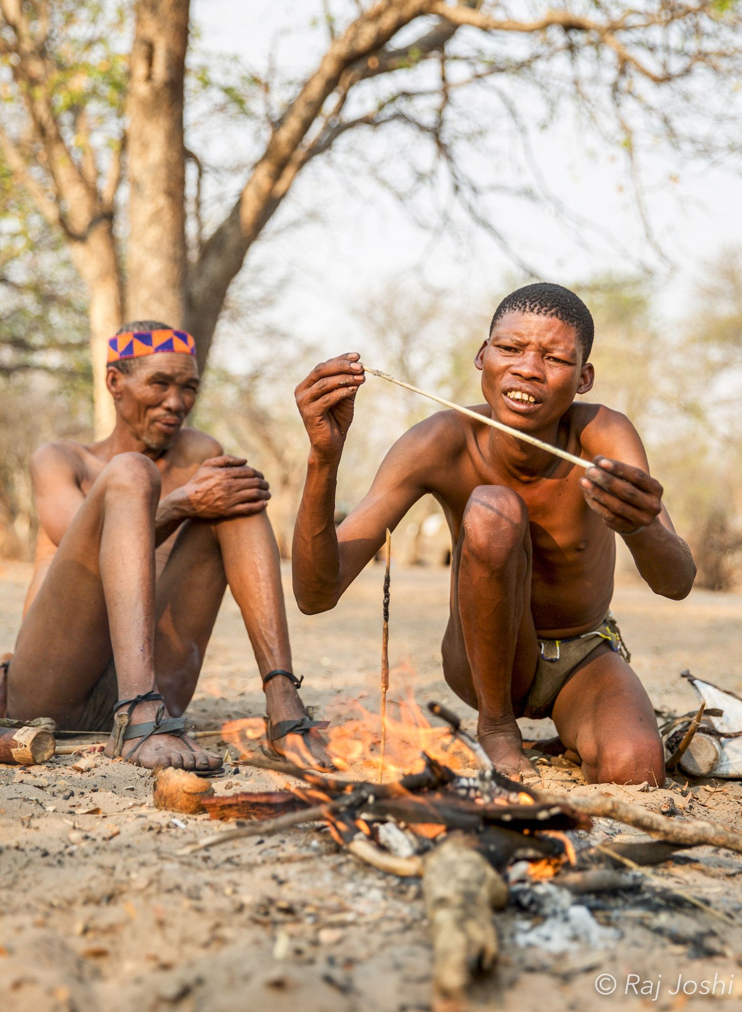 Two San guides crouched making fire the traditional way in dry scrub