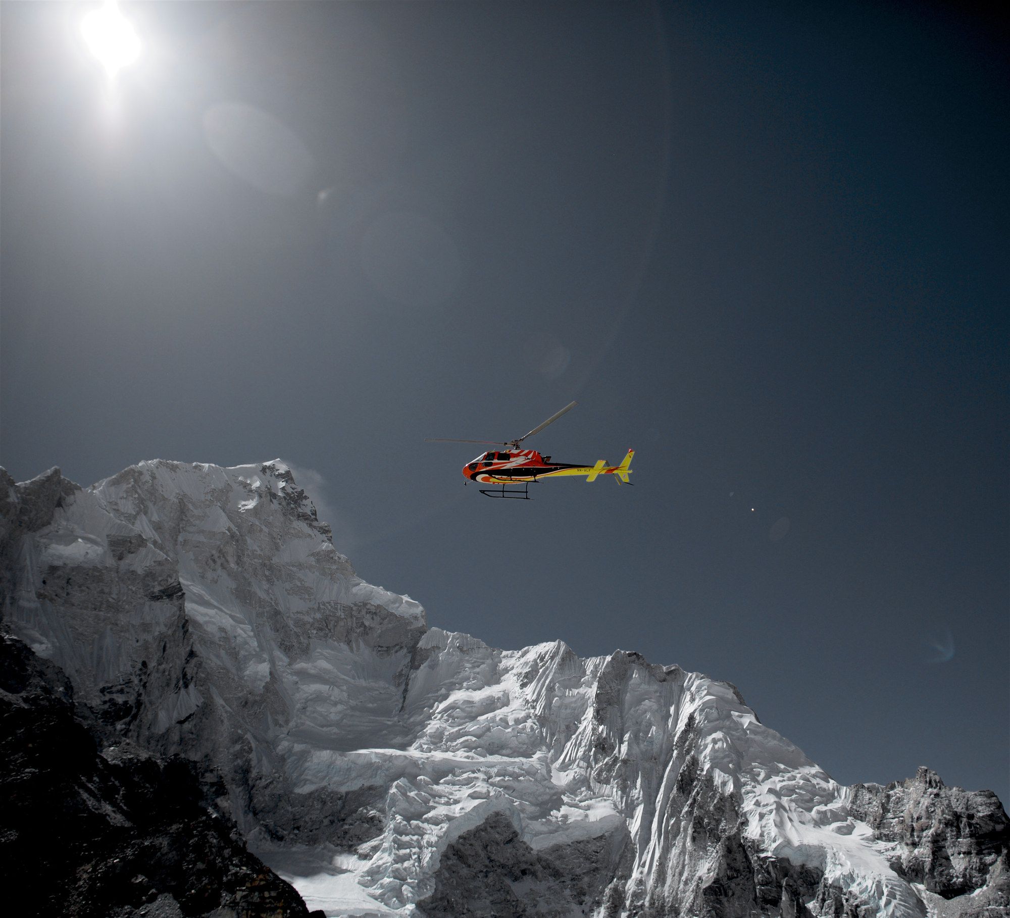 A small rescue helicopter dwarfed between vast snow-covered mountain walls