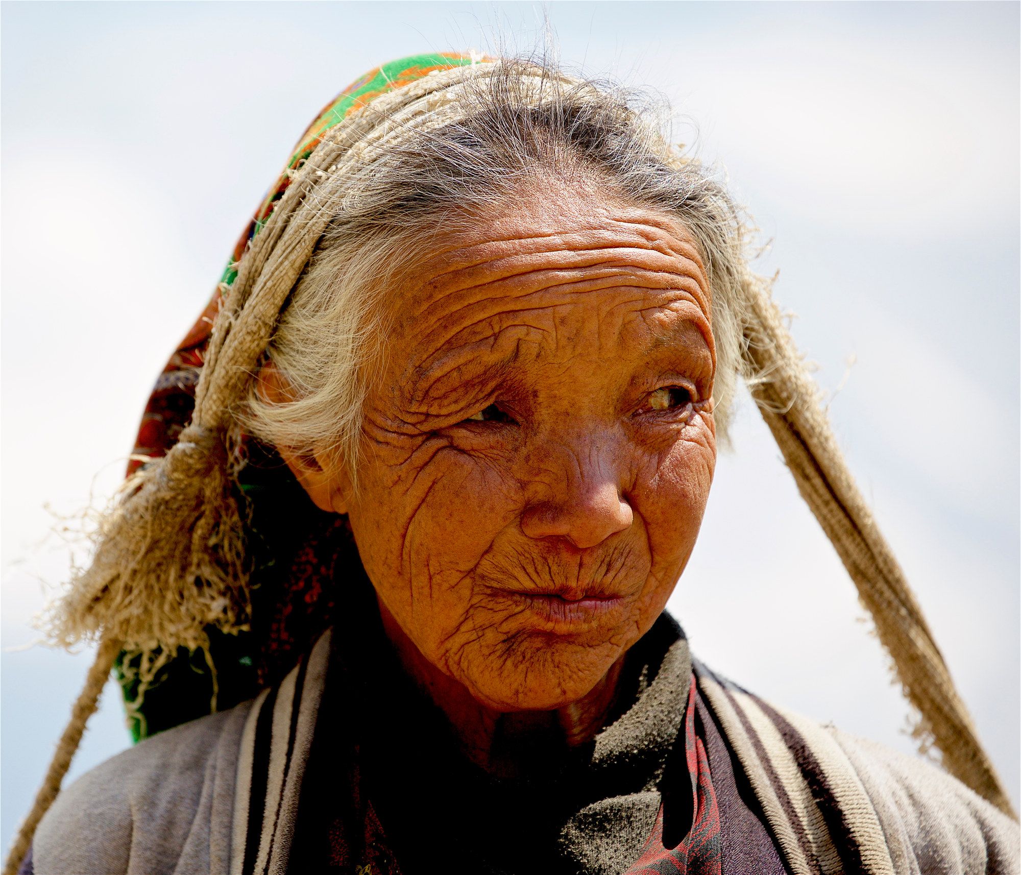 Close portrait of an elderly woman with a weathered face and pale headscarf
