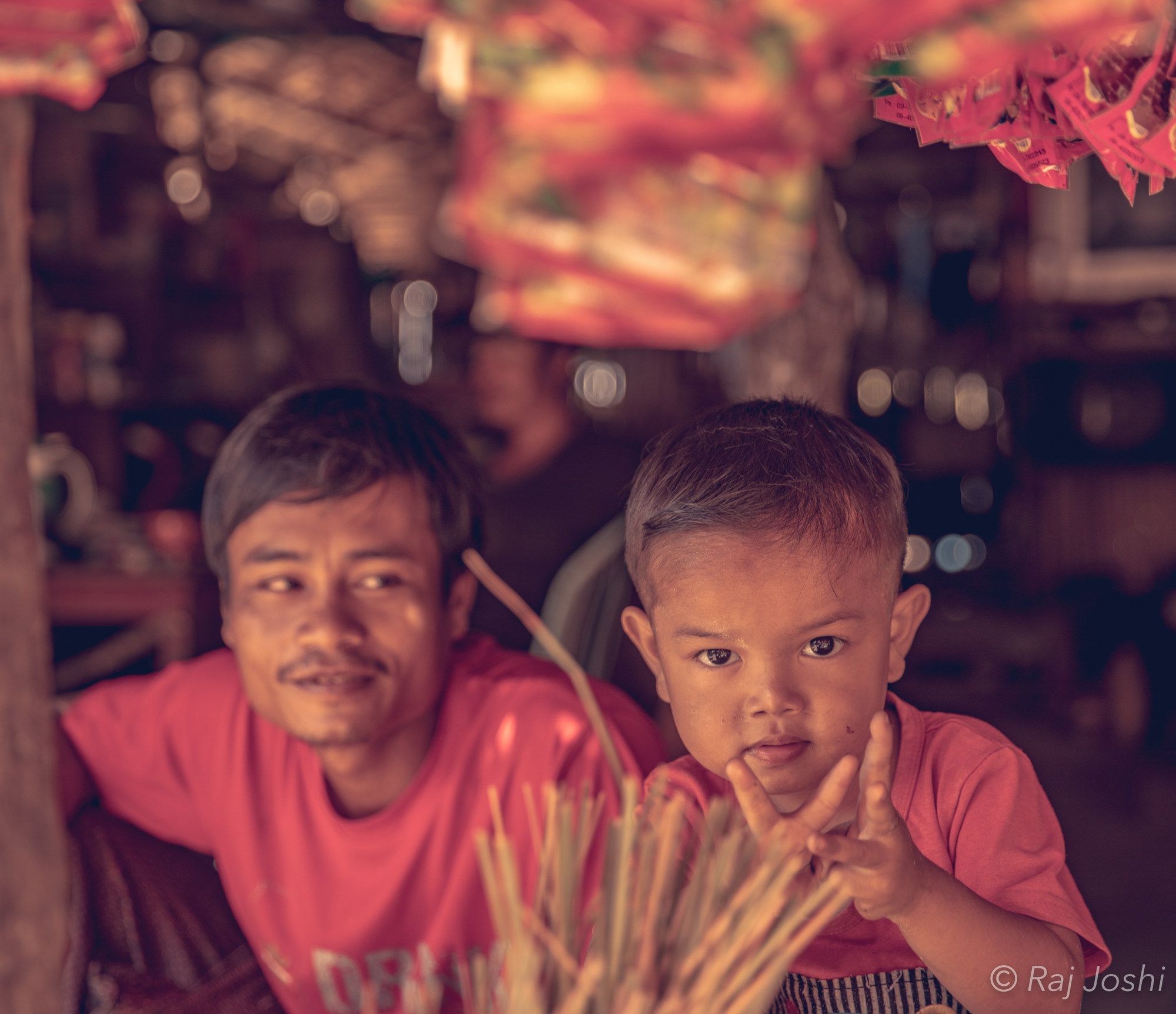 A father and his young son at a family market stall, both in red