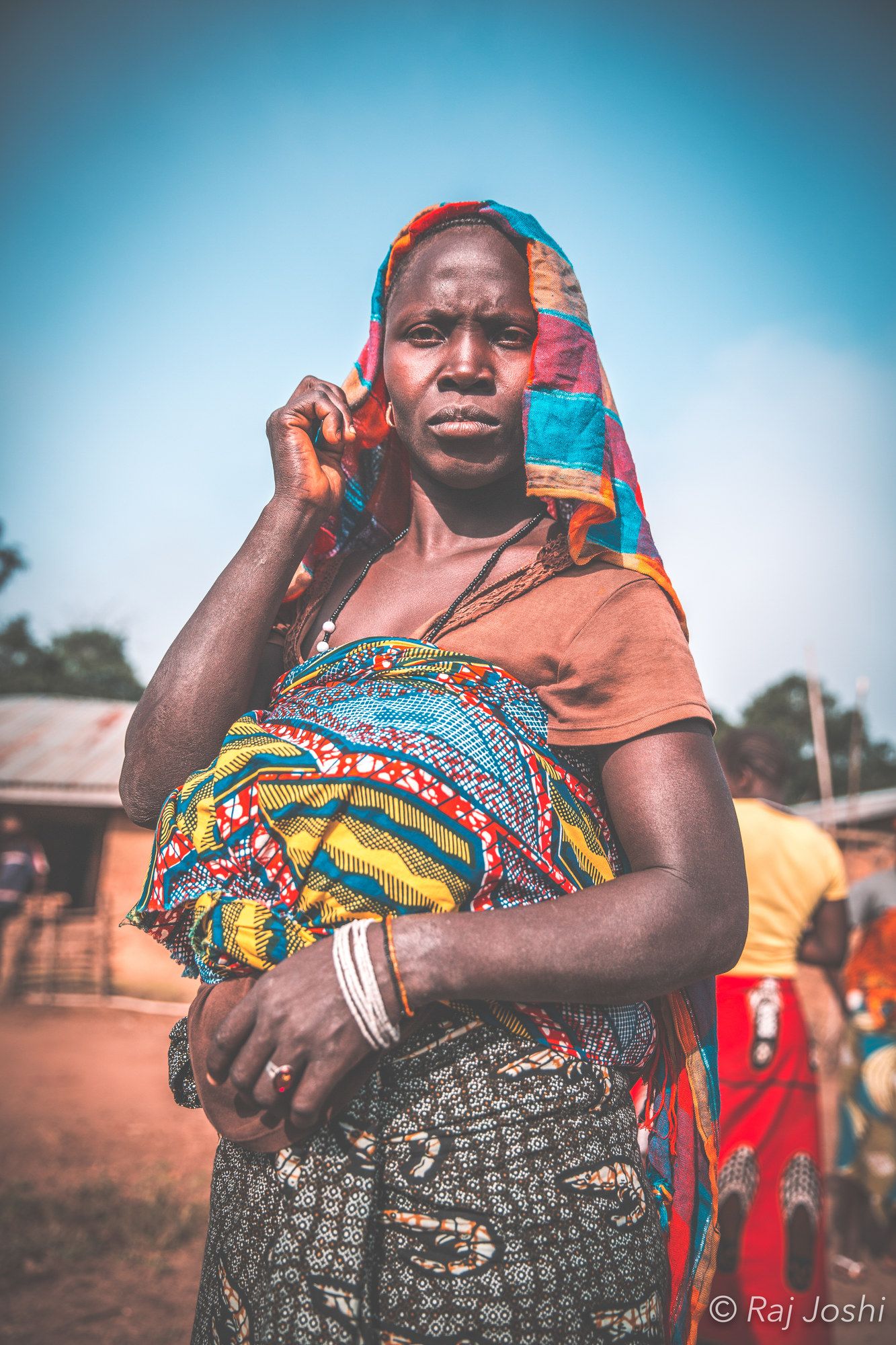 A mother in bright patterned cloth holding her child against a painted wall