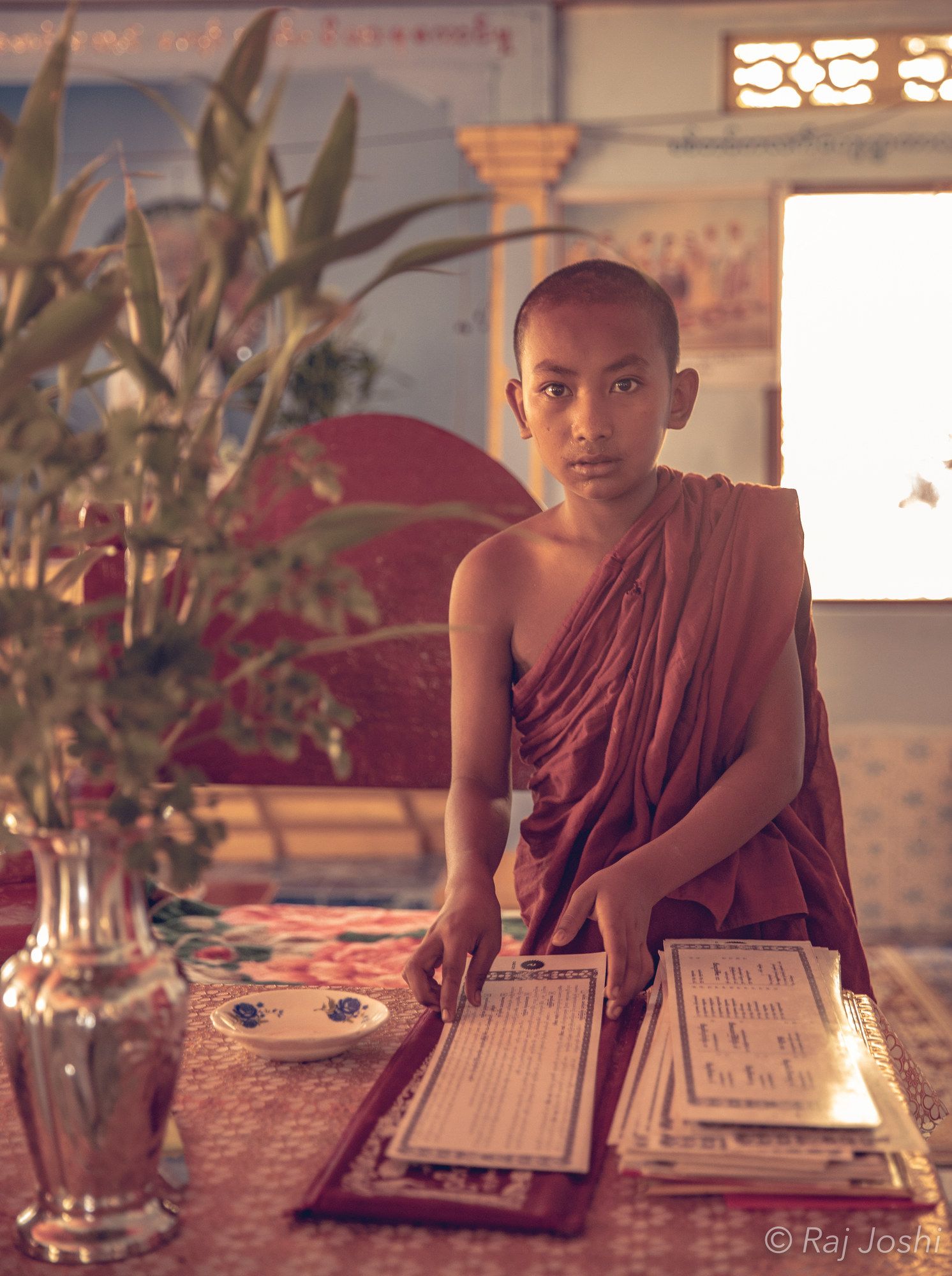 A young novice monk in maroon robes in the cool light of a monastery