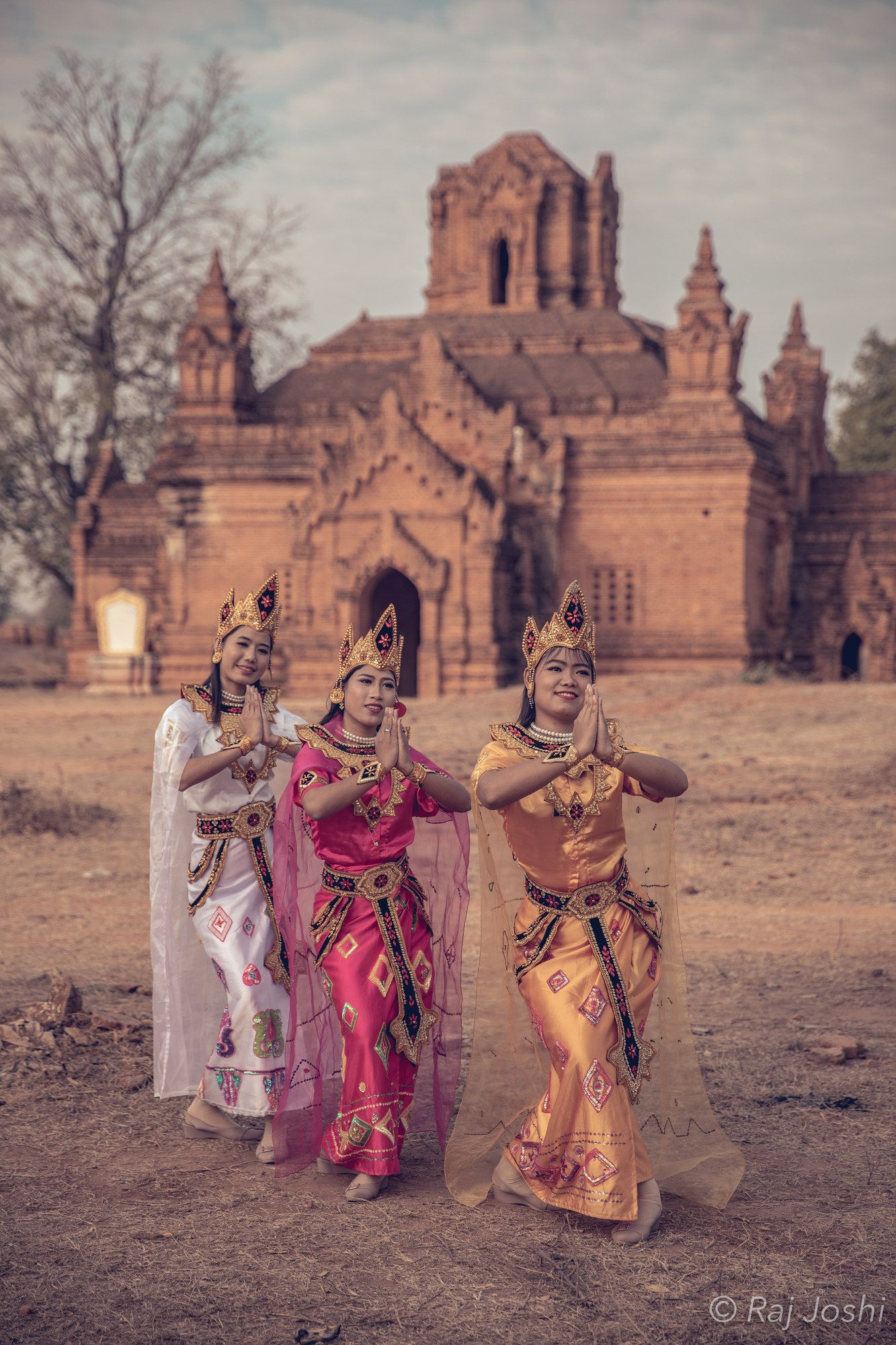 Two women in bright festival dress standing before a weathered brick stupa