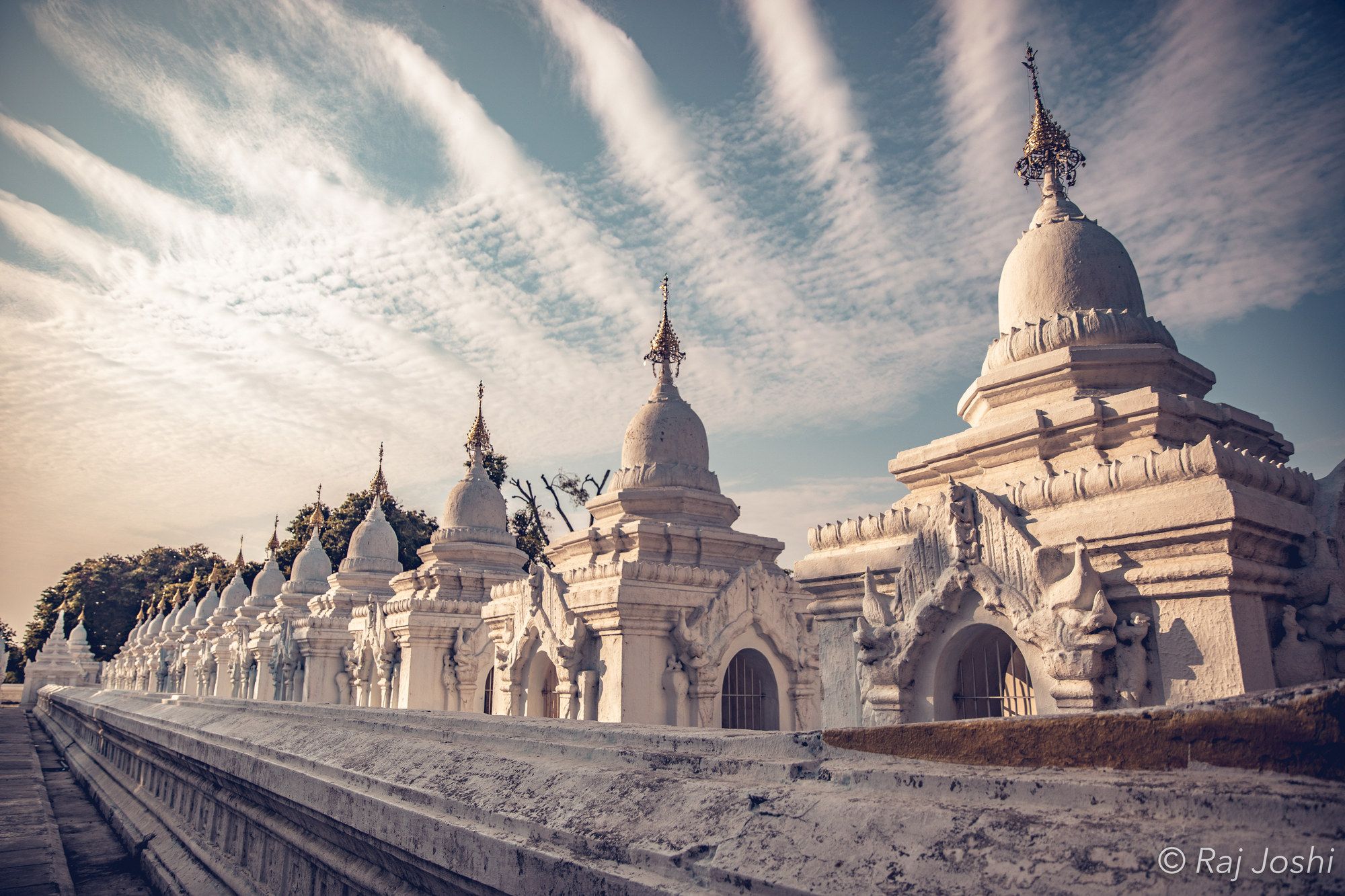 The white tiered terraces of a hilltop pagoda leading up toward a dramatic sky