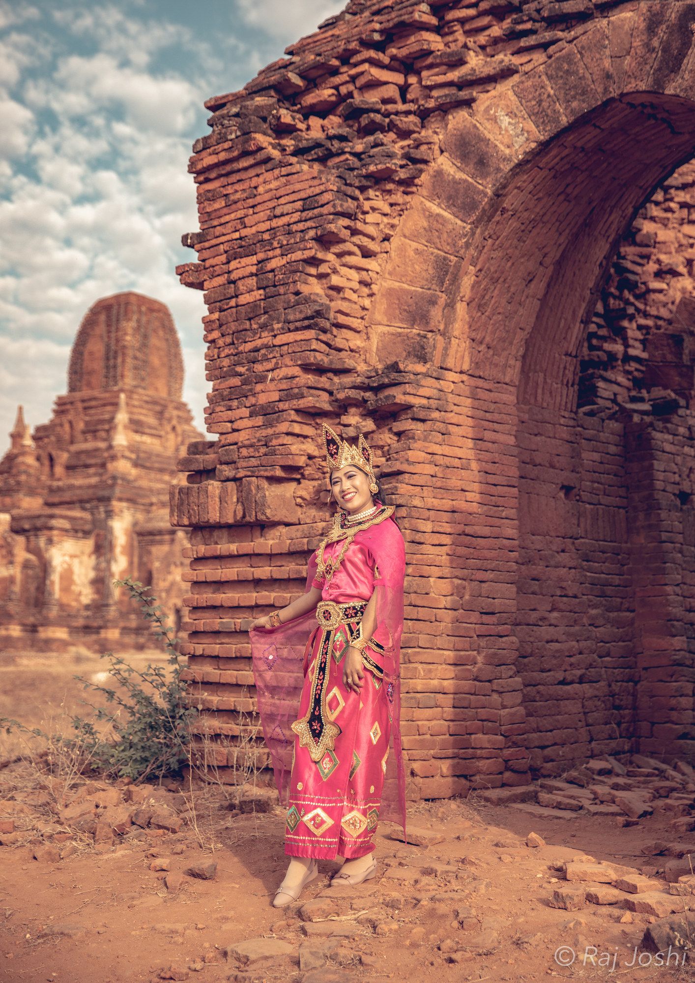 A pilgrim in a pink sari walking through a tall ancient brick archway