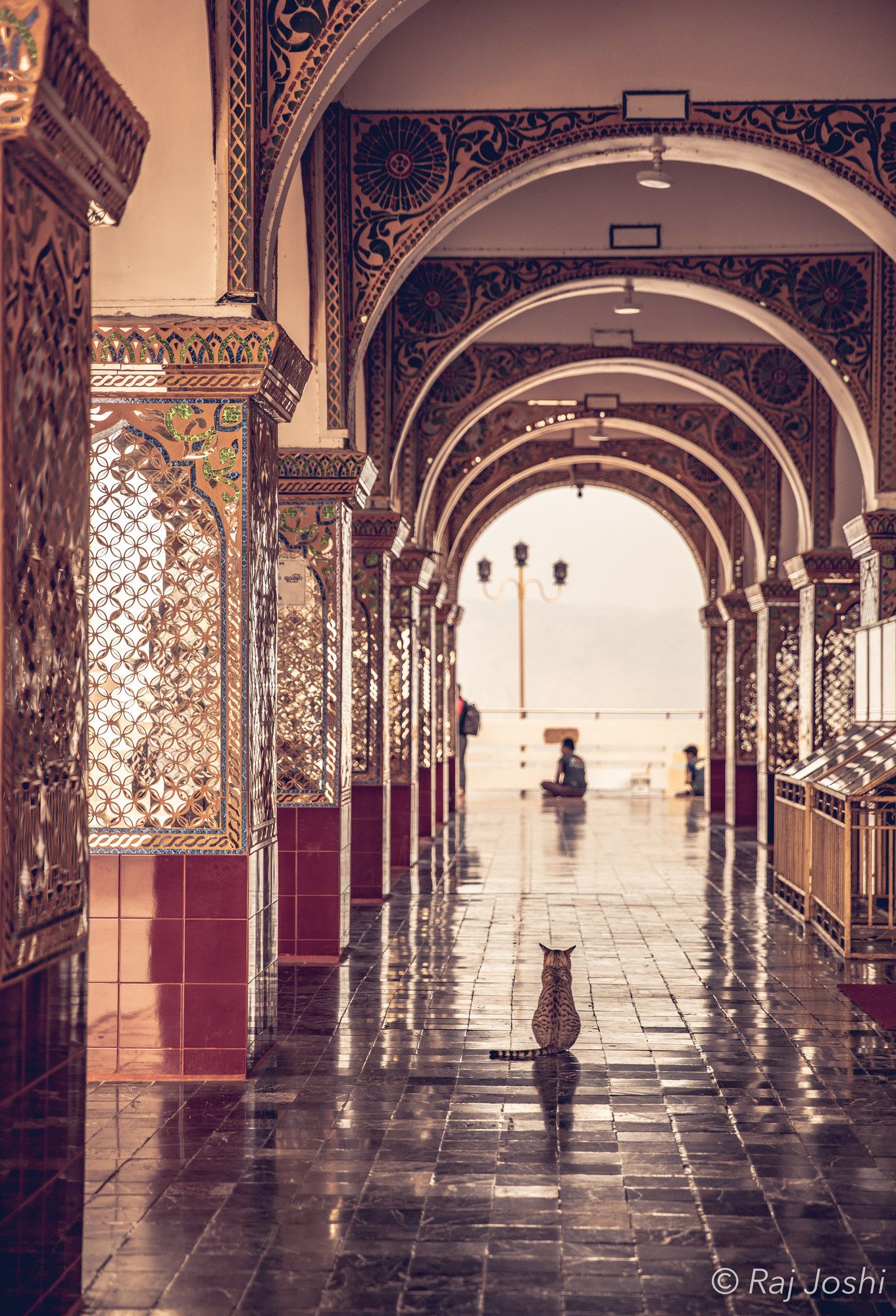 Light falling through a long, receding temple colonnade with a distant figure